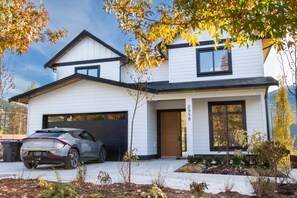 Una moderna casa a due piani con garage, vialetto e giardino anteriore curato con diverse piante.