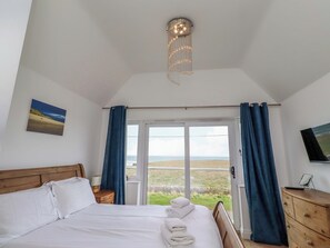 Ein Schlafzimmer mit Bett, Nachttisch, Lampe, Fernseher an der Wand und Blick ins Freie.
