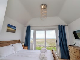 Un dormitorio con cama, mesita de noche, lámpara, televisor en la pared y vistas al exterior.