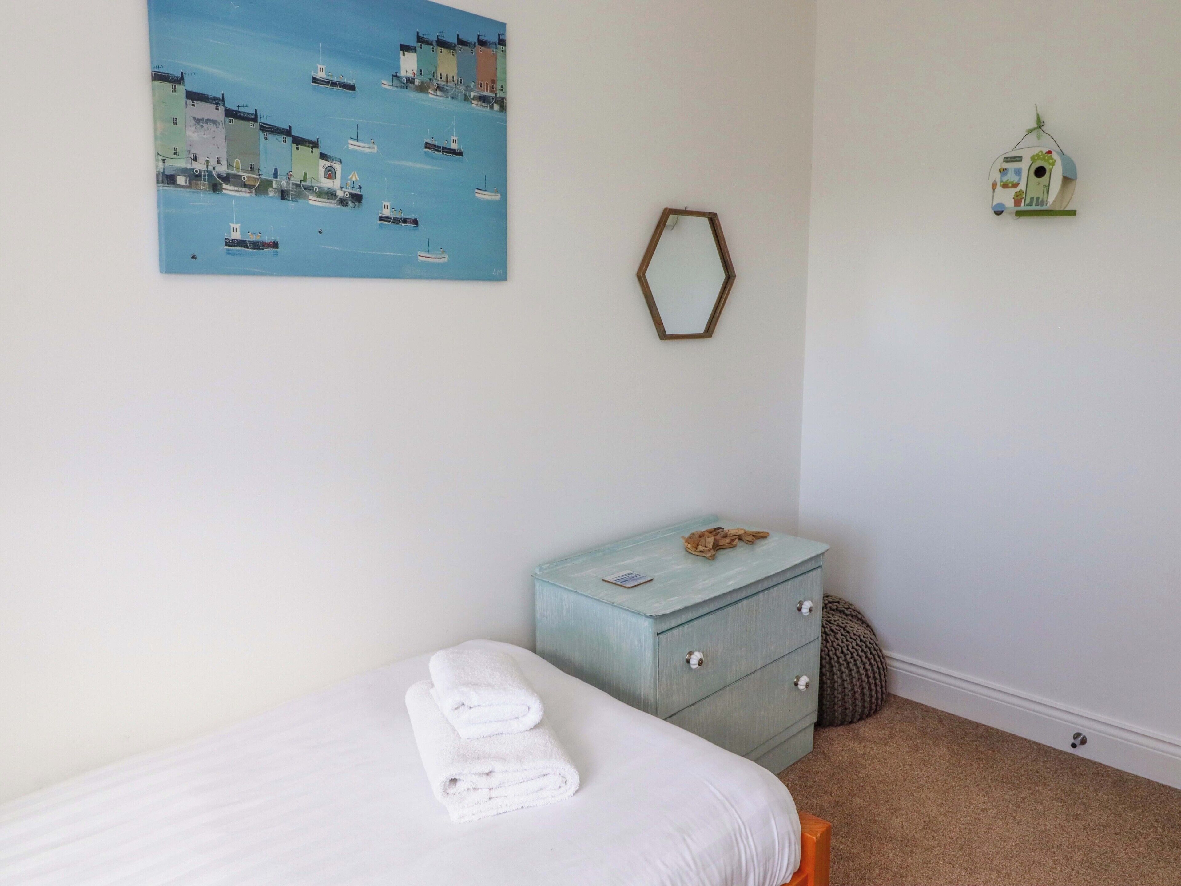 A bedroom with a bed, a dresser, a painting, a mirror, and a birdhouse.
