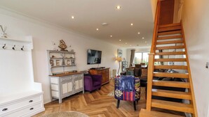 A spacious living area with a herringbone floor pattern, a wooden staircase, and a television mounted on the wall. - Farne Cottage (Chathill)