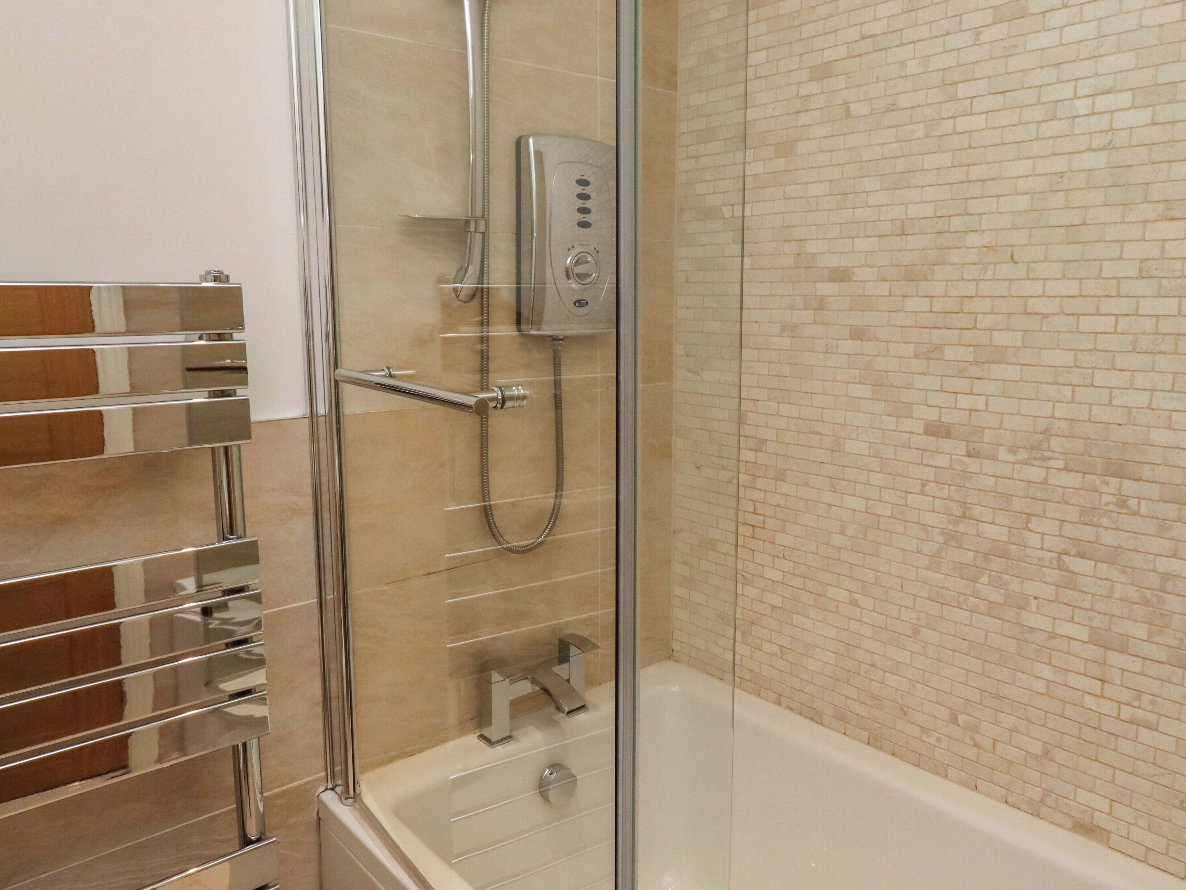 Une salle de bain avec une douche à parois de verre, une baignoire et un mur recouvert de carreaux.