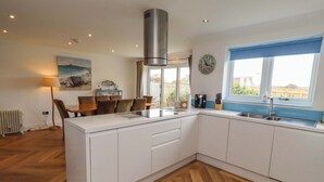 A modern kitchen with white cabinets, a herringbone wood floor, a built-in island, and a window with a view. - Farne Cottage (Chathill)