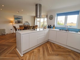 Una cocina moderna con armarios blancos, piso de madera en patrón de espiga y una isla integrada, con ventana y vistas.