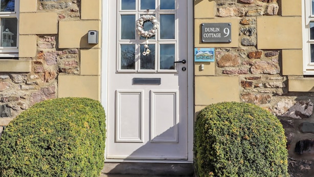 A white door with a glass panel, a stone wall, and a sign reading 'DUNLIN COTTAGE 9'. - No9 Budle Sands (Bamburgh)