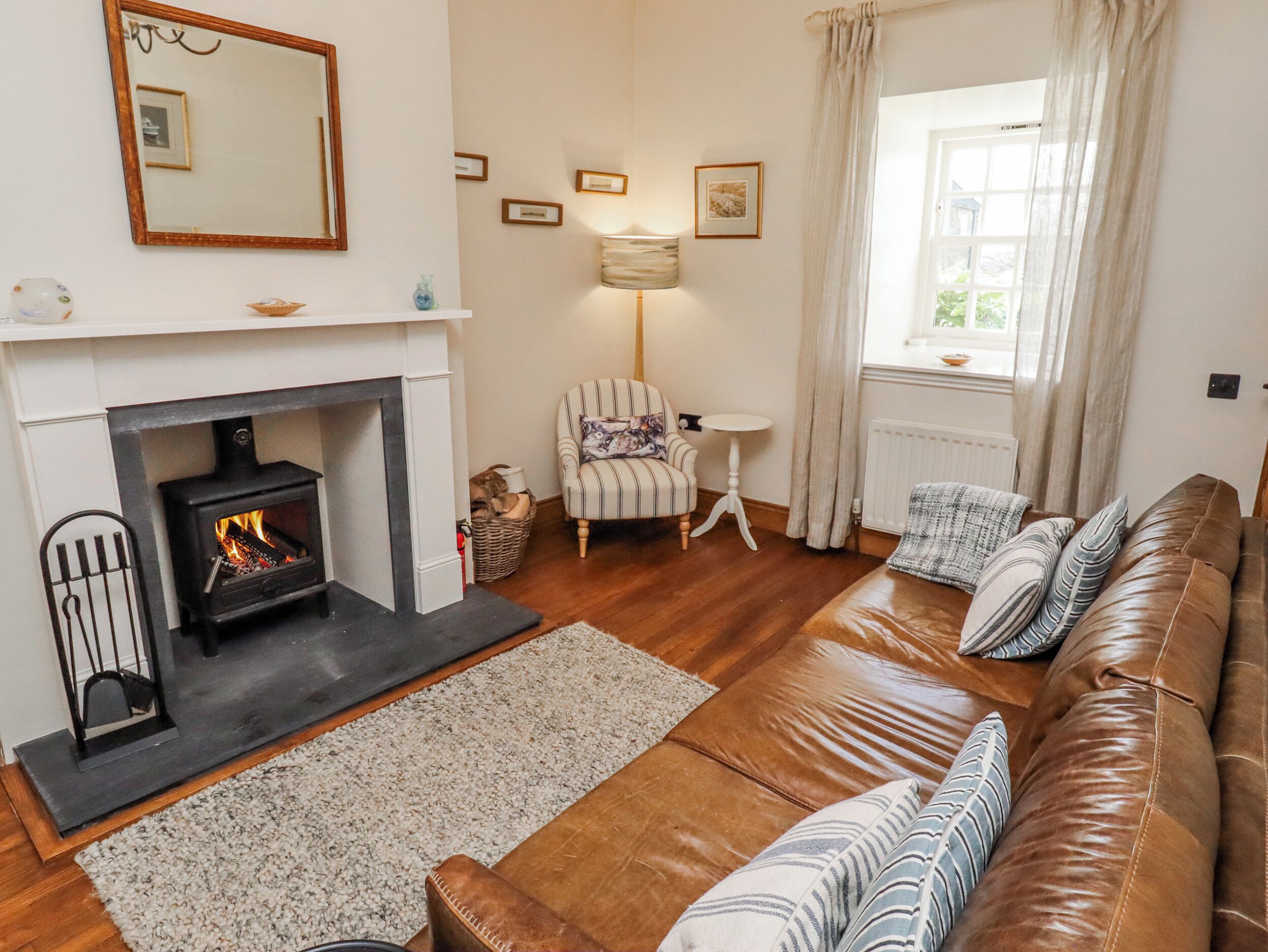 A living room with a fireplace, a sofa, a chair, a lamp, and a window with curtains.