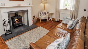A living room with a fireplace, a sofa, a chair, a lamp, and a window with curtains. - No9 Budle Sands (Bamburgh)