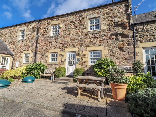 A stone building with multiple windows, a door, and a small outdoor seating area with a bench and a table.