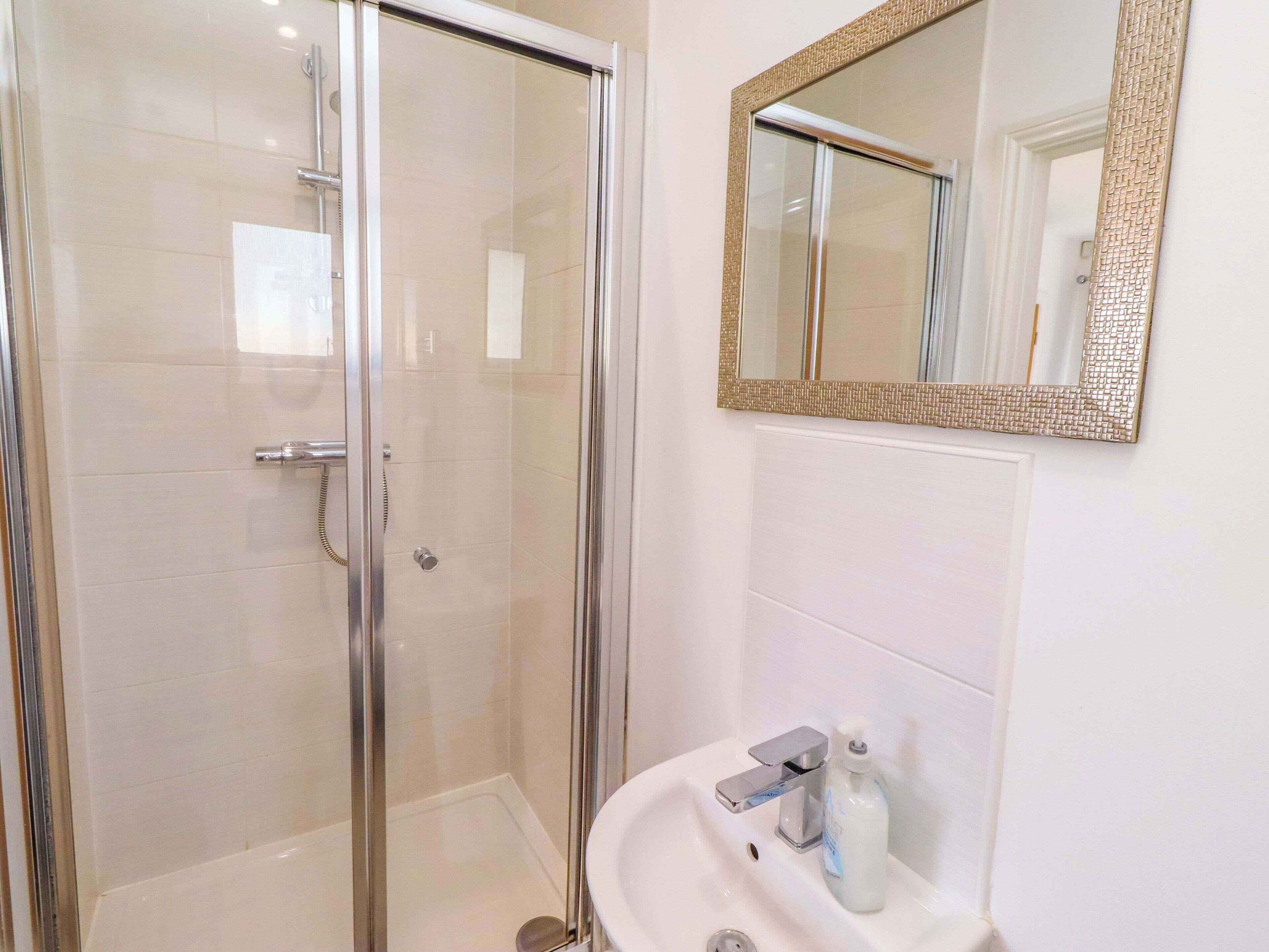 Une salle de bain avec une douche à parois de verre, un lavabo avec un miroir et un flacon de savon.