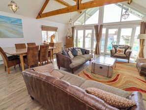 A spacious living area with a leather sofa, a dining table with chairs, a coffee table, and a view through large windows. - Spindrifter (Chathill)