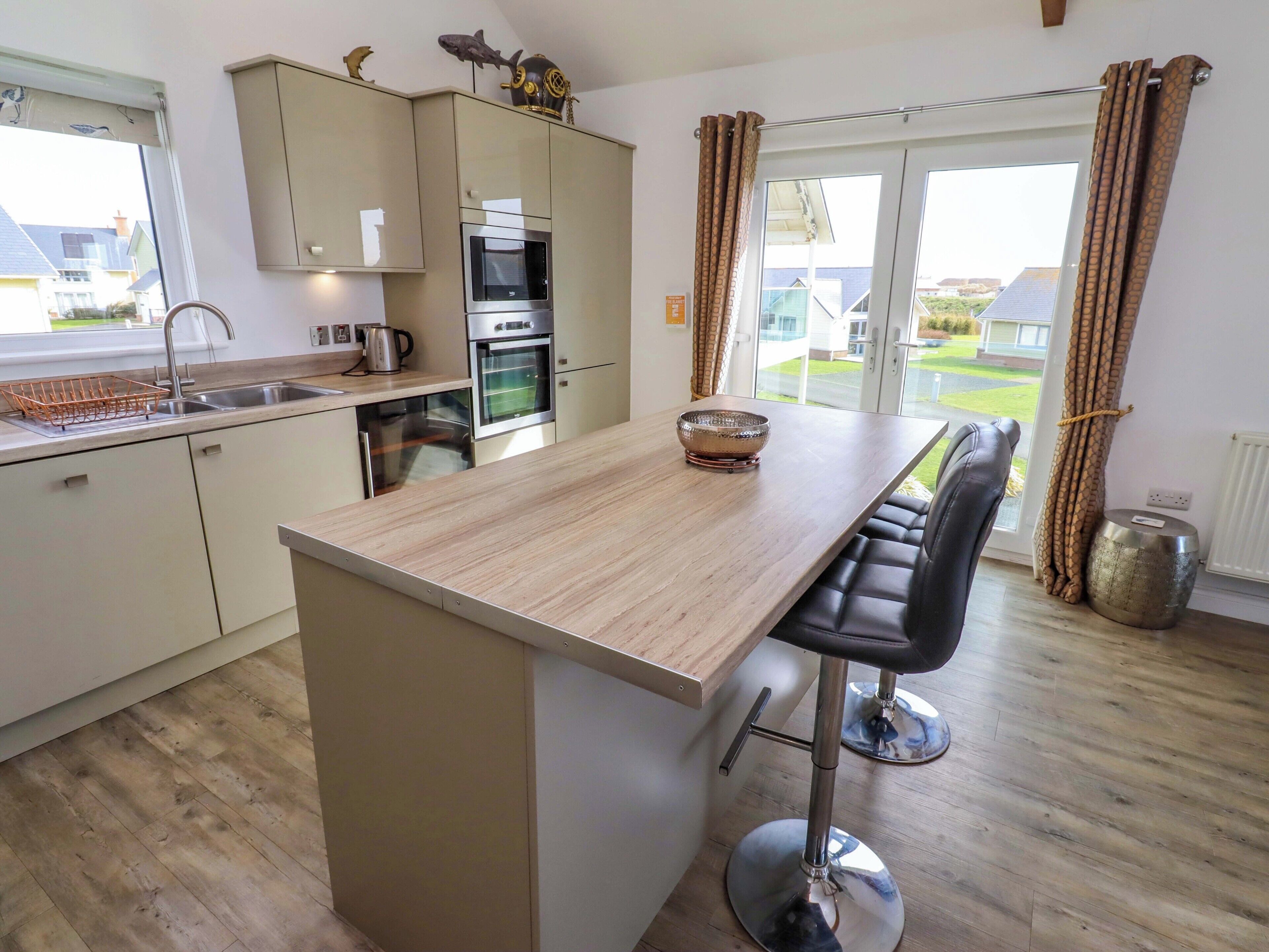 A modern kitchen with a central island, bar stools, and a view of the outside.