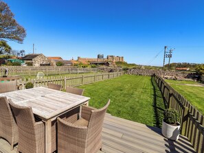 A wooden deck with wicker furniture, a stone wall, and a view of a historic building in the background.