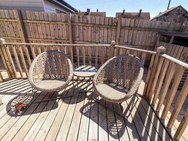 A wooden deck with two wicker chairs and a small table.