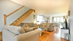A spacious living room with a wooden staircase, a kitchen in the background, and a dining area. - Portland (Chathill)