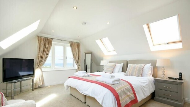 A modern bedroom with a large bed, a TV, and a desk. - Portland (Chathill)