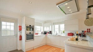 A modern kitchen with white cabinets, a built-in oven, a microwave, and a large island with a sink. - Portland (Chathill)