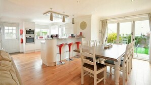 A modern kitchen with a central island, bar stools, and a dining table with chairs. - Portland (Chathill)