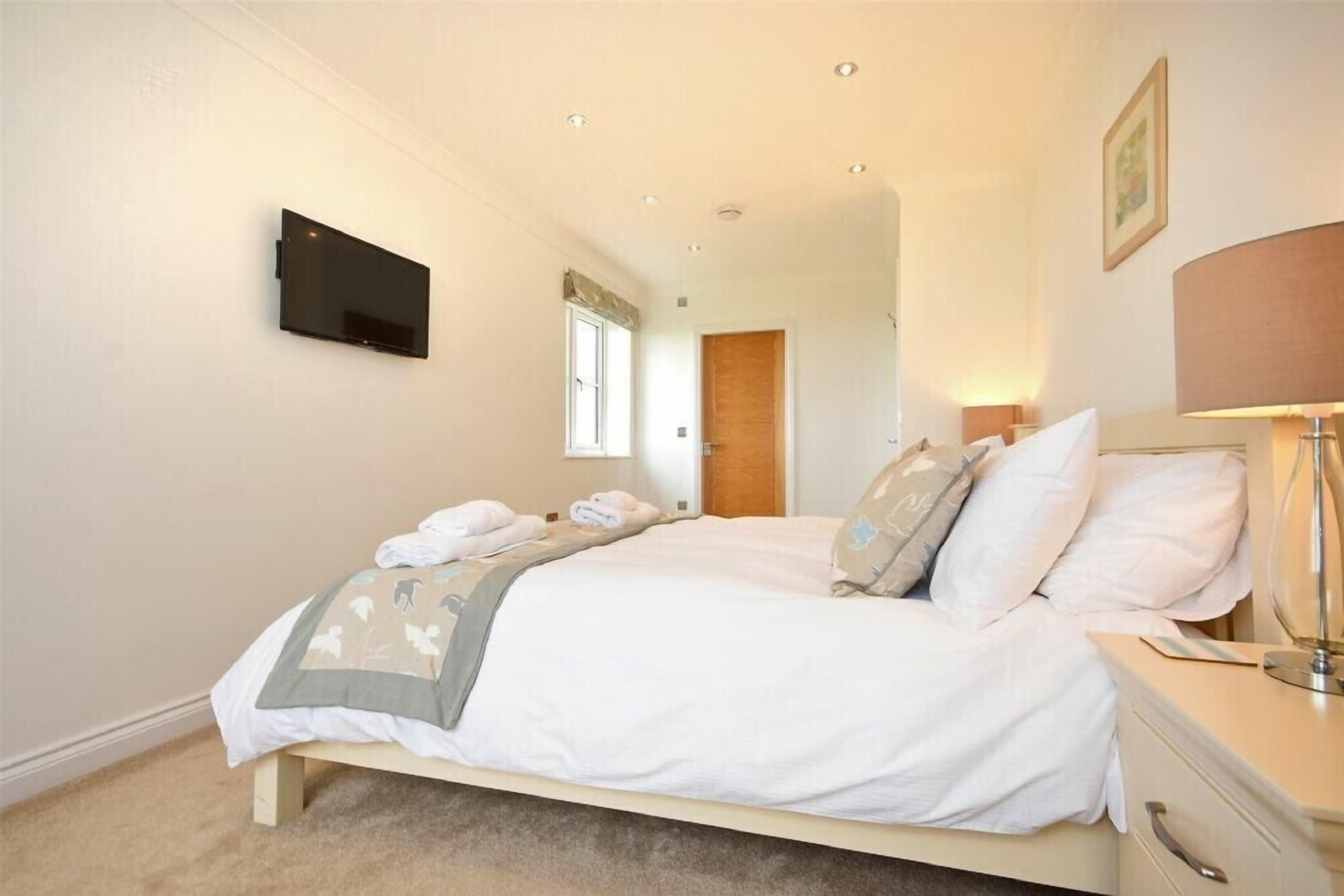 A bedroom with a bed, bedside table, lamp, and a flat-screen TV mounted on the wall.