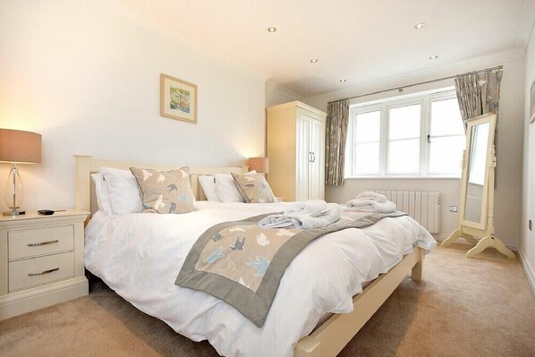 A bedroom with a bed, bedside tables, a window with curtains, a radiator, and a mirror. - Portland (Chathill)