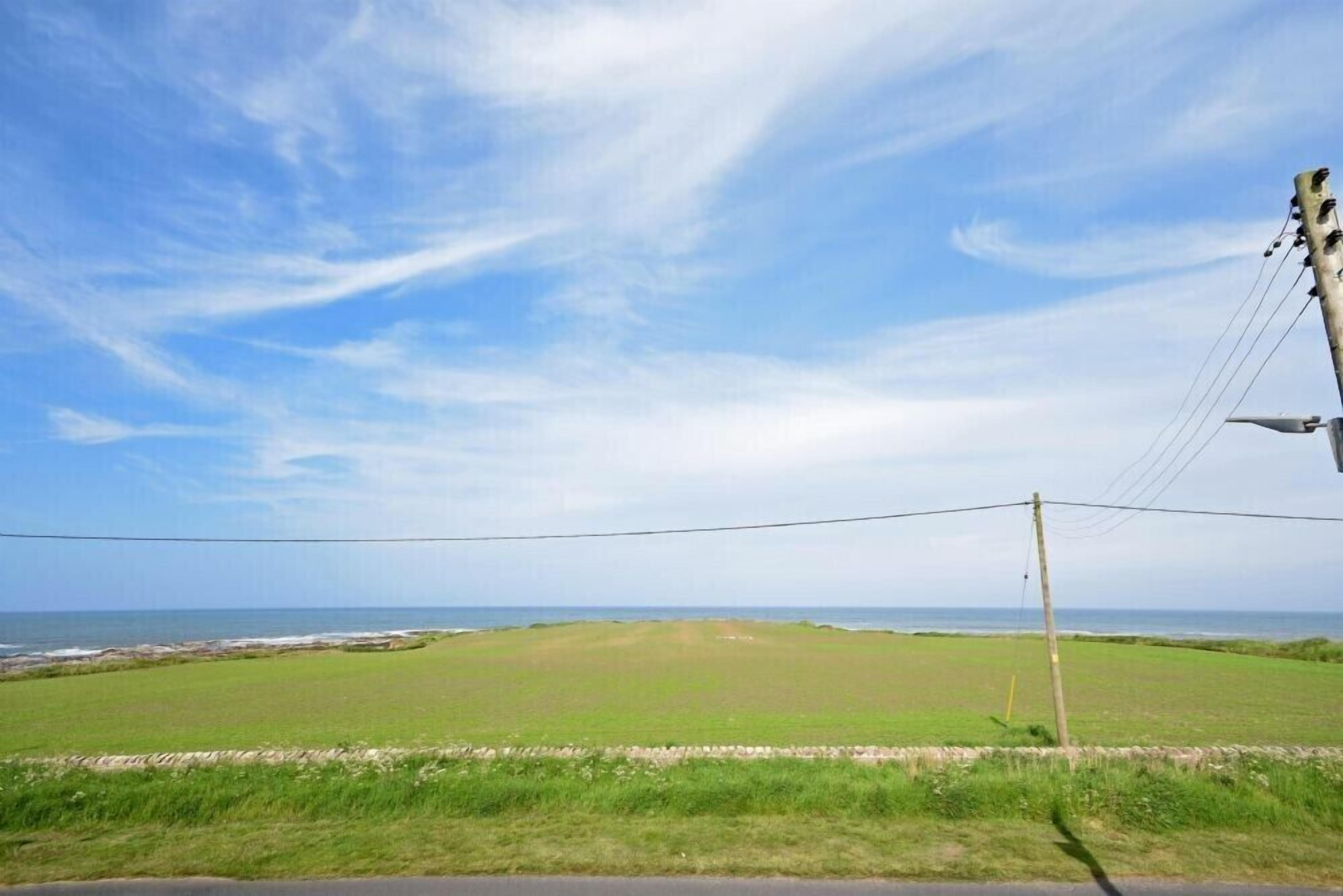 A coastal road with a grassy field and a view of the sea.