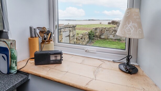 Een kamer met een houten bureau, een Sony radio, een lamp en een raam met uitzicht op een stenen muur en een grasveld.