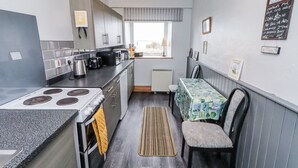 Een kleine keuken met een fornuis, broodrooster en waterkoker, een eettafel met stoelen en een raam met uitzicht.