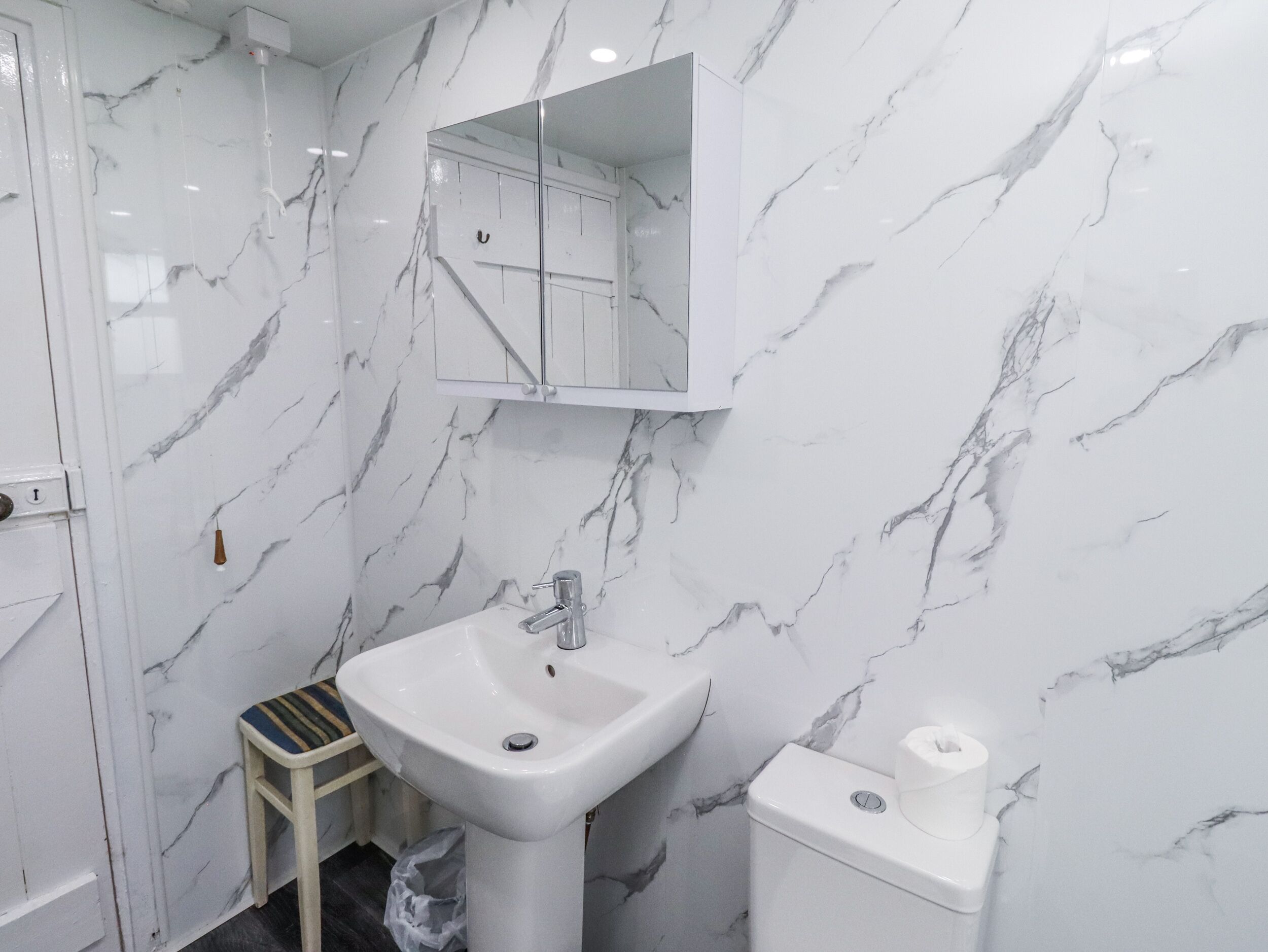 A bathroom with a marble wall, a sink, a mirror, and a toilet.