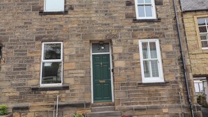 A stone building with three windows, a green door, and a visible number '54'. - Strandline (Alnwick)