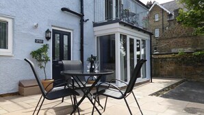 A patio with a round table and four chairs, a potted plant, and a door with a number plate. - Schooner Court No2 (Alnwick)