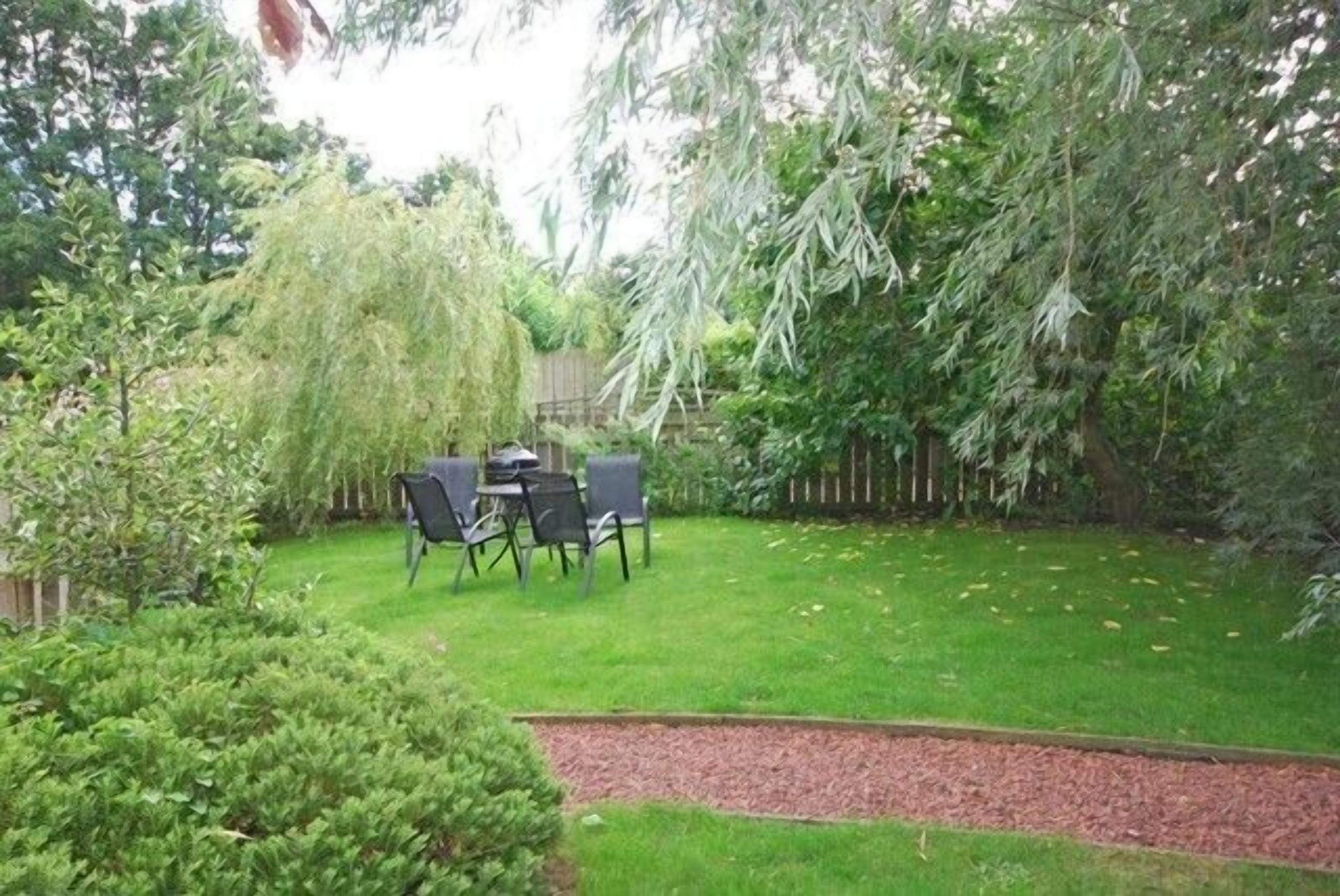 Un patio trasero con un pequeño porche, una cerca de madera y varias plantas.