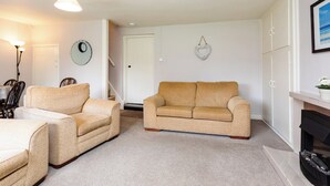 Ein Wohnzimmer mit beigefarbenem Sofa, einem passenden Sessel, einem Kamin und einer Wanduhr.