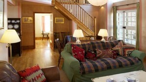 A cozy living room with a green sofa, a wooden staircase, and a dining area. - Kirknowe (Hawick)