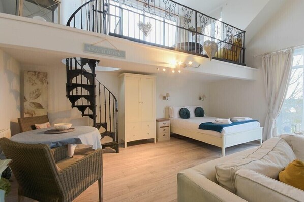 A spacious bedroom with a bed, a small table, and a chair. There is a staircase leading to an upper level.