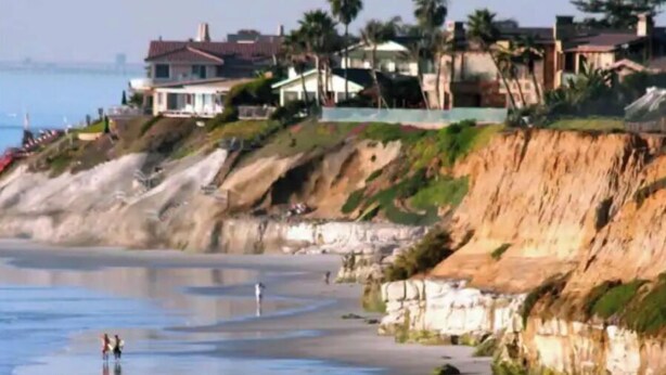 Una propiedad costera con playa, casas al borde del acantilado y vistas al océano.