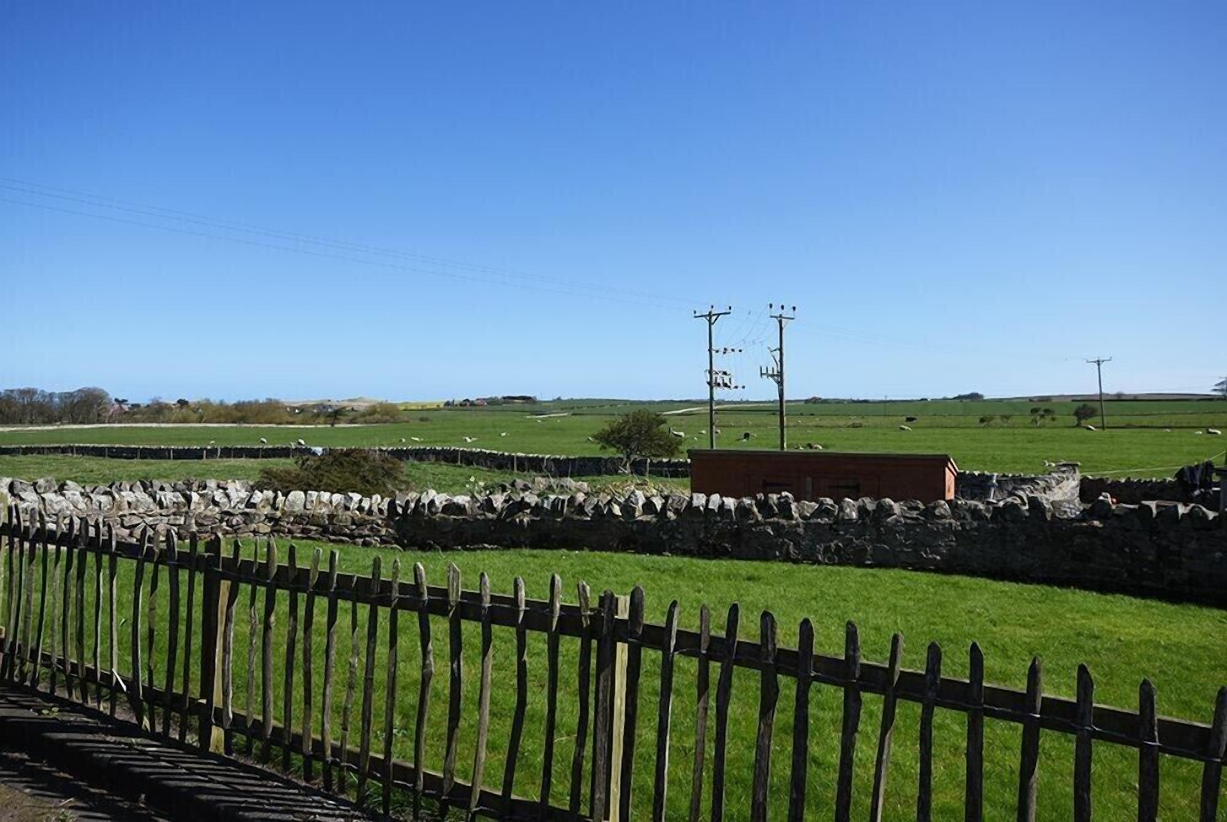 A rural landscape with stone walls, a wooden fence, and a small building.