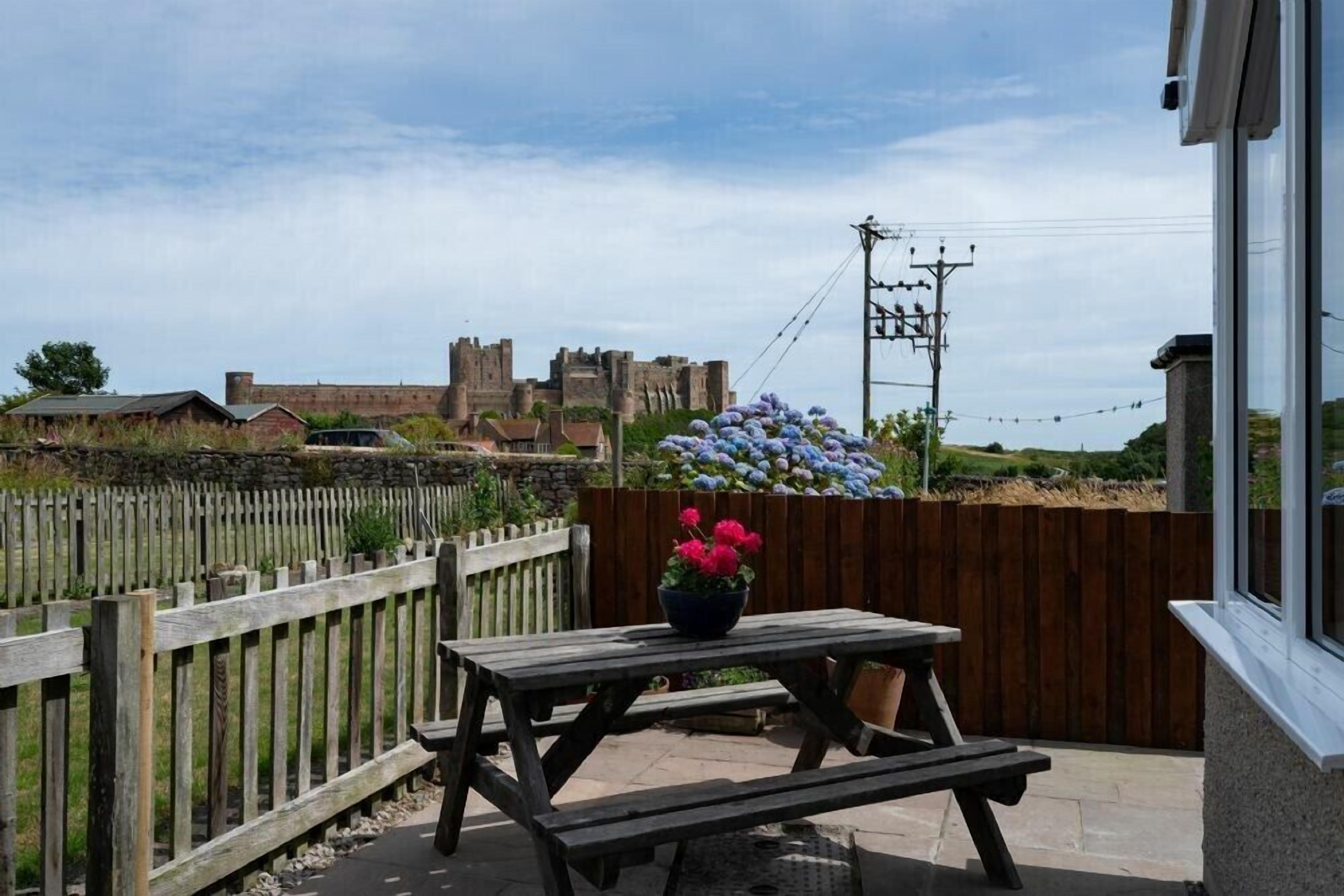 A wooden picnic table with a flower pot, a wooden fence, and a view of a castle-like structure in the background.