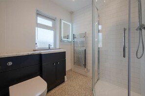 A bathroom with a toilet, a sink, a mirror, a towel rack, and a shower with glass doors. - Castle View (Bamburgh)