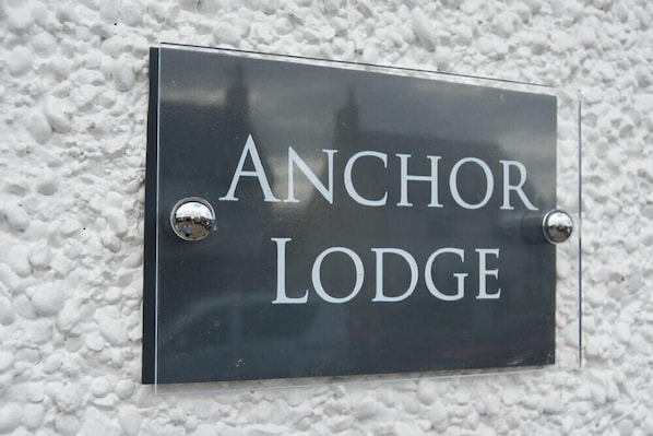 A metal sign with the words "ANCHOR LODGE" mounted on a textured wall. - Anchor Lodge (Seahouses)