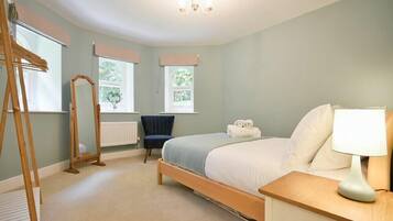 A bedroom with a bed, bedside table, lamp, chair, windows, radiator, and a ladder.