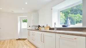 Uma cozinha moderna com armários brancos, bancada de madeira e janela com vista para o verde.