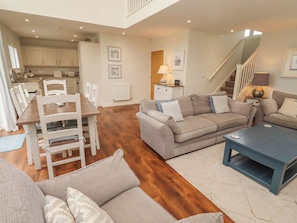 A spacious living area with a dining table, sofas, and a staircase leading to an upper floor. - The Beach Hut (Chathill)
