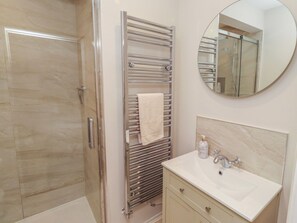 Ein Badezimmer mit Duschabtür aus Glas, einem Handtuchhalter mit weißem Handtuch, einem runden Spiegel und einem Waschbecken mit Marmorplatte.
