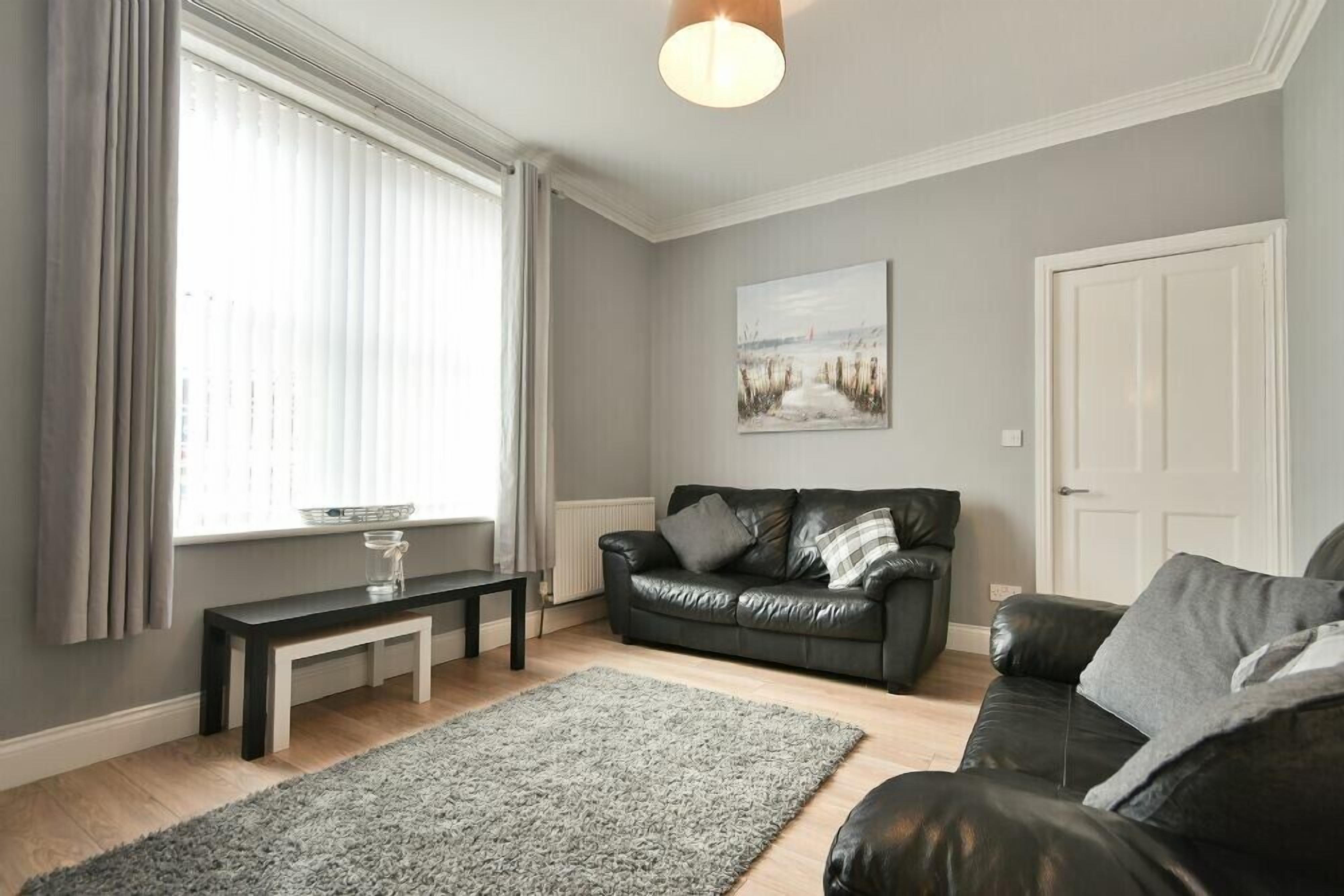 A living room with a black leather sofa, a grey rug, a wooden coffee table, and a painting on the wall.
