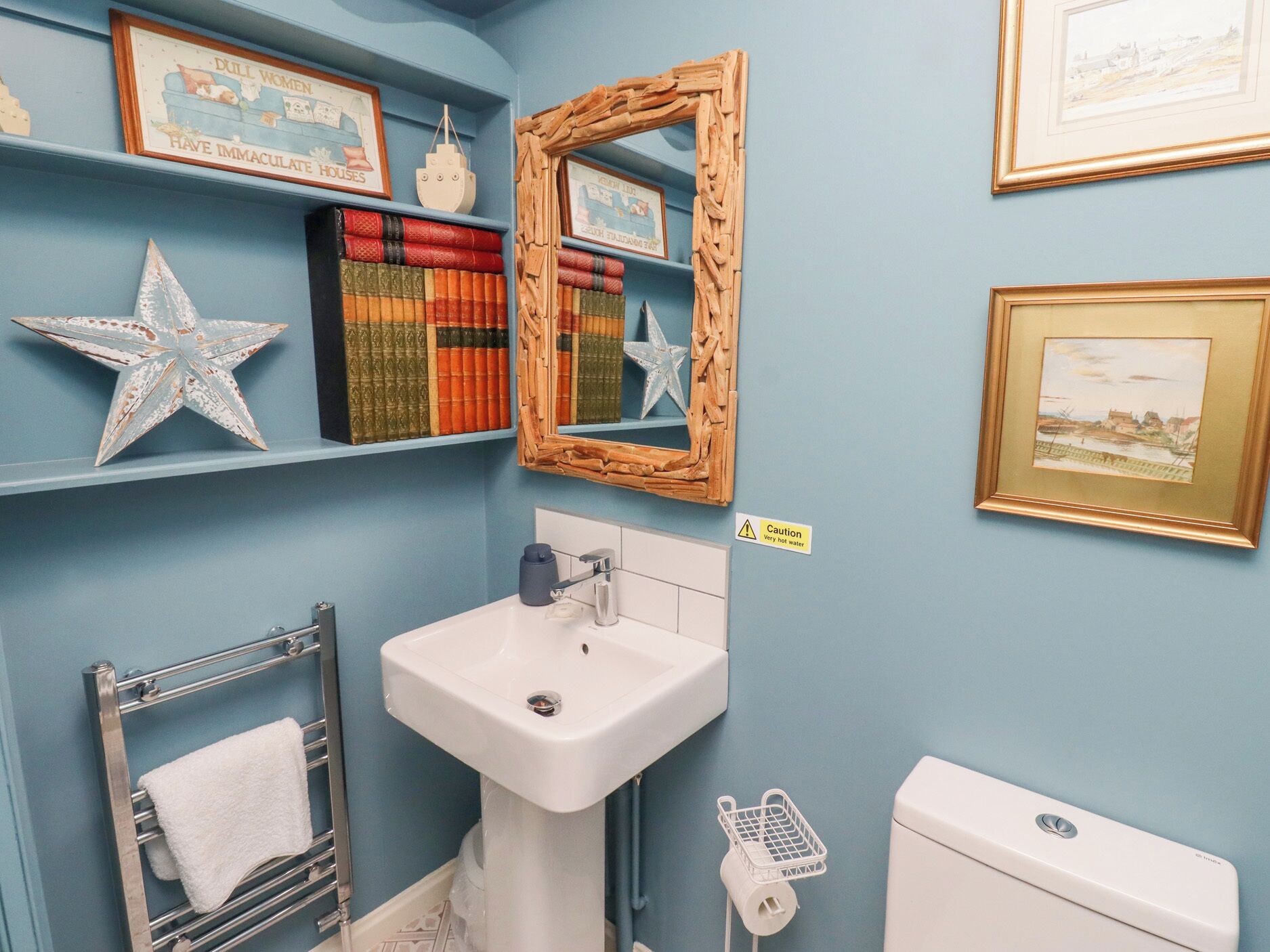 Ein Badezimmer mit weißem Waschbecken, Handtuchhalter, Toilette und Regalen mit Büchern und Dekoration.