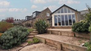 Ein Haus mit einer Stein-Fassade, einem großen Wintergarten und einem gepflegten Garten mit verschiedenen Pflanzen und einem Kiesweg.