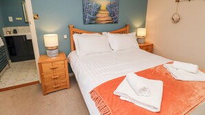 Ein Schlafzimmer mit einem Bett, zwei Nachttischen, einem Schminktisch und einem Bild an der Wand. Ein Badezimmer ist durch eine offene Tür zu sehen.