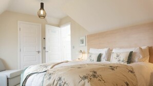 Ein Schlafzimmer mit einem großen Bett, einem Nachttisch, einer Lampe und einer Tür.