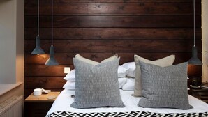 Un dormitorio con cabecera de madera, dos lámparas de noche y dos almohadas estampadas sobre una cama con colcha de diseño geométrico.