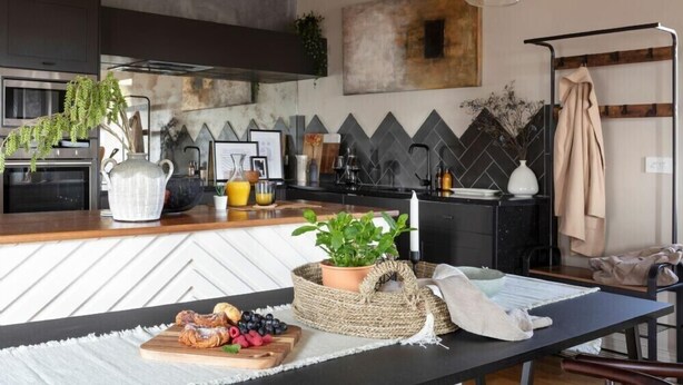 Una cocina moderna con encimera negra, una mesa de comedor de madera y diversos electrodomésticos.