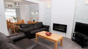 A living room with a leather sofa, a wooden coffee table, a flat-screen TV, and a dining area with wooden chairs and a table. - Bay View (Morpeth)